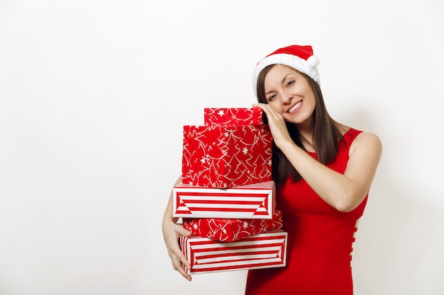 Hermosa mujer feliz joven caucásica con sonrisa encantadora vestida con vestido rojo y sombrero de Navidad con cajas de regalo sobre fondo blanco. Niña de Santa con presente aislado. Concepto de vacaciones de año nuevo 2018