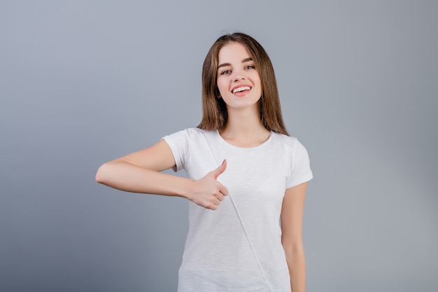 Hermosa mujer feliz mostrando pulgares arriba aislado sobre gris