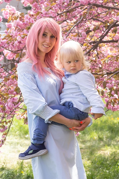 Hermosa mujer feliz con un niño pequeño cerca de un árbol floreciente de sakura rosa Concepto de primavera