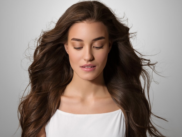 Hermosa mujer feliz con el pelo largo en vestido blanco sobre fondo de color gris.Retrato de modelo joven