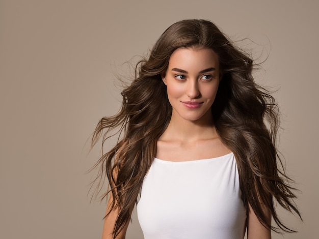 Hermosa mujer feliz con el pelo largo en vestido blanco sobre fondo de color marrón.Retrato de modelo joven