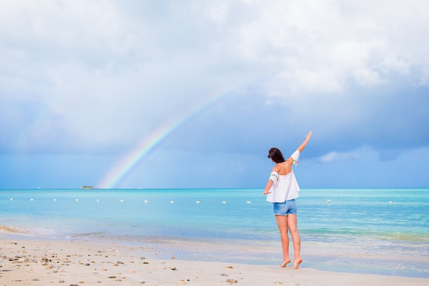 Hermosa mujer feliz en la playa con hermoso arco iris sobre el mar