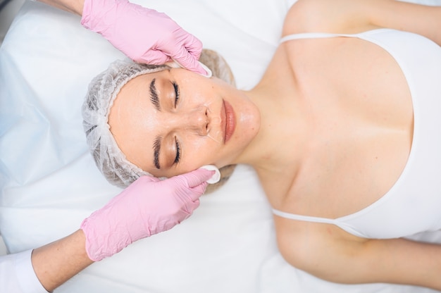 Hermosa mujer feliz recibiendo tratamiento de spa cosmetóloga en el rostro de mujer de limpieza de salón de belleza