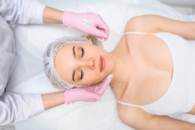 Hermosa mujer feliz recibiendo tratamiento de spa cosmetóloga en salón de belleza con un guante rosa