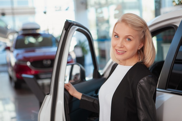 Hermosa mujer feliz sonriendo alegremente, comprando un auto nuevo en el concesionario, copie el espacio