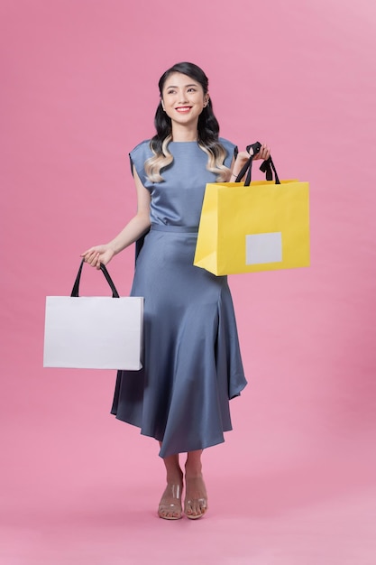 Hermosa mujer feliz sosteniendo muchas bolsas de compras coloridas aisladas en un fondo rosa