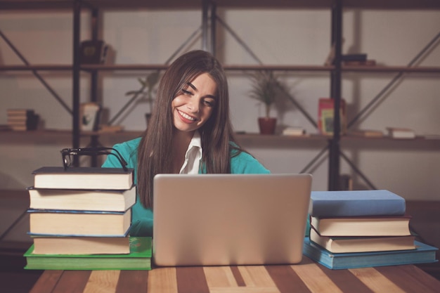 Foto hermosa mujer está feliz por su exitoso trabajo con una computadora portátil y libros en la mesa de madera