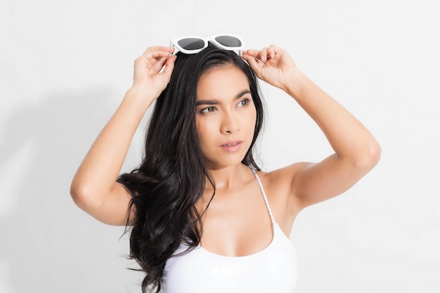 Hermosa mujer feliz con vestido de traje de baño blanco y sosteniendo gafas de sol blancas en sesión de estudio de moda de verano de concepto aislado sobre fondo blanco.