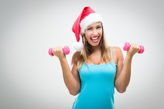 Hermosa mujer fitness con sombrero de santa haciendo ejercicio entrenando brazos levantando pesas.