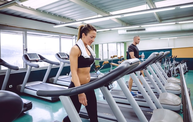 Hermosa mujer fitness con una toalla sobre su cuello entrenando en una  caminadora en el gimnasio