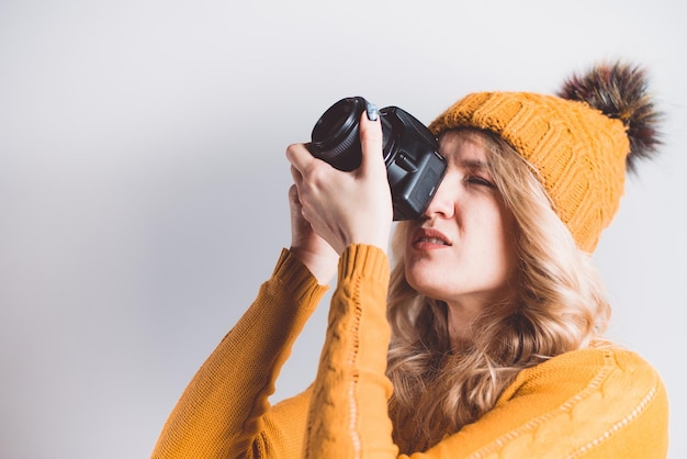 Una hermosa mujer fotógrafa con un gorro de punto es fotografiada con una cámara en sus manos en un estudio fotográfico