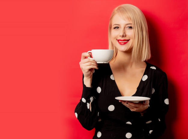 Hermosa mujer francesa sostiene una taza de café en la pared roja
