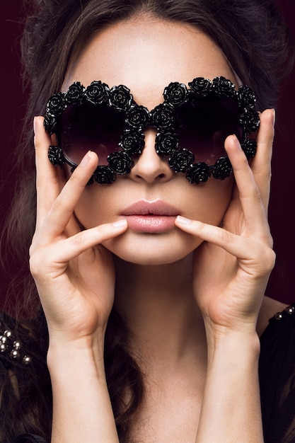 Hermosa mujer en gafas de sol oscuras, con rizos y maquillaje de noche