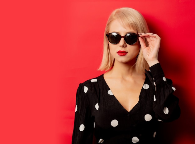 Hermosa mujer con gafas de sol en la pared roja