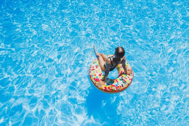 Hermosa mujer con gafas de sol en la piscina flota en un anillo de natación inflable en un traje de baño negro foto de verano fotografía de natación fotos de mujer de verano