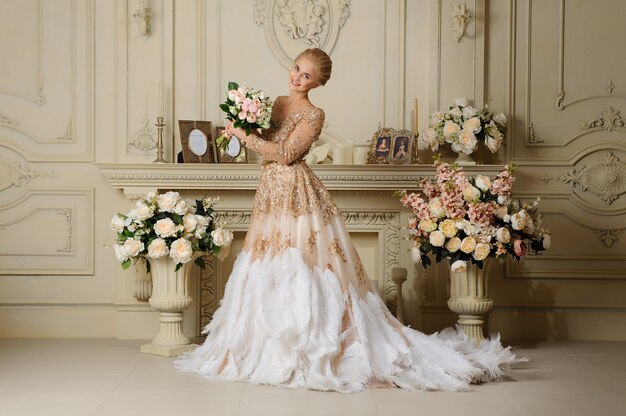 Hermosa mujer glamorosa en vestido beige en interior.