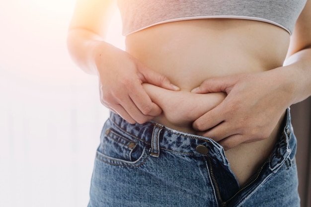 Hermosa mujer gorda con cinta métrica. Usa su mano para exprimir el exceso de grasa que está aislado en un fondo blanco. Quiere perder peso, el concepto de cirugía y descomponer la grasa bajo el