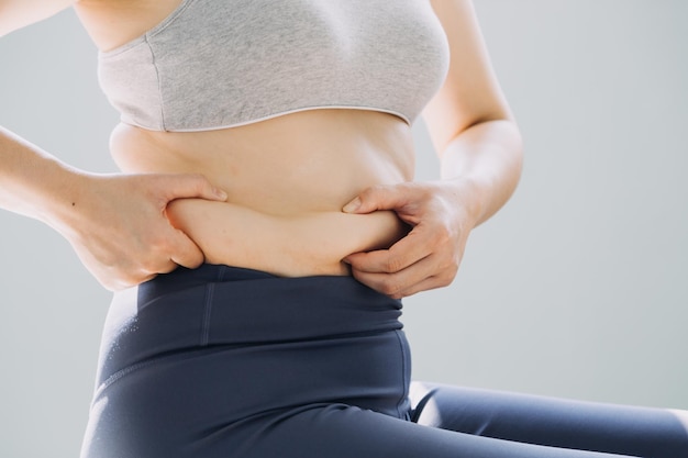 Hermosa mujer gorda con cinta métrica. Usa su mano para exprimir el exceso de grasa que está aislado en un fondo blanco. Quiere perder peso, el concepto de cirugía y descomponer la grasa bajo el