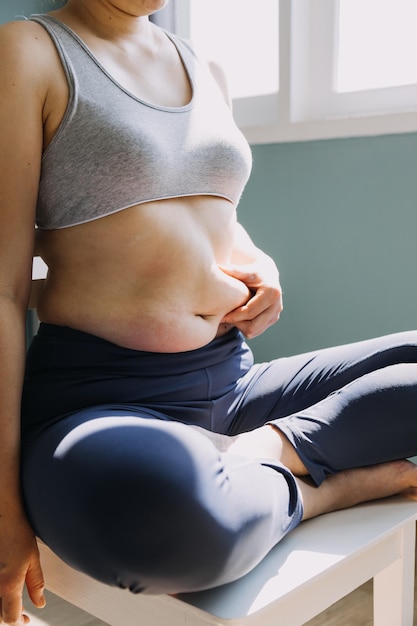 Hermosa mujer gorda con cinta métrica. Usa su mano para exprimir el exceso de grasa que está aislado en un fondo blanco. Quiere perder peso, el concepto de cirugía y descomponer la grasa bajo el