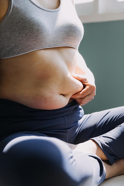 Hermosa mujer gorda con cinta métrica. Usa su mano para exprimir el exceso de grasa que está aislado en un fondo blanco. Quiere perder peso, el concepto de cirugía y descomponer la grasa bajo el