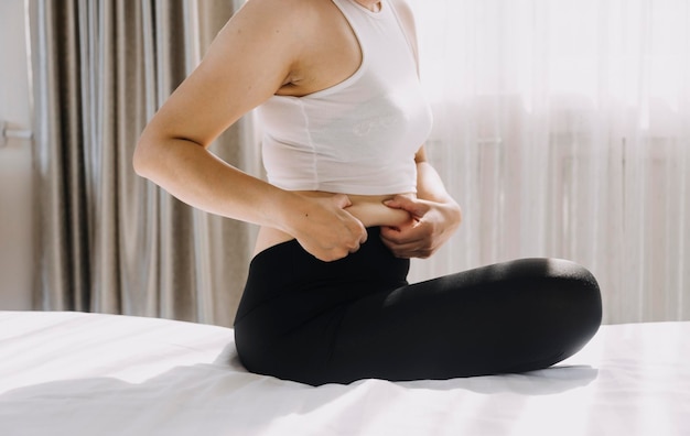 Hermosa mujer gorda con cinta métrica. Usa su mano para exprimir el exceso de grasa que está aislado en un fondo blanco. Quiere perder peso, el concepto de cirugía y descomponer la grasa bajo el