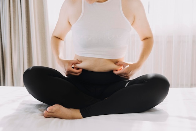 Hermosa mujer gorda con cinta métrica. Usa su mano para exprimir el exceso de grasa que está aislado en un fondo blanco. Quiere perder peso, el concepto de cirugía y descomponer la grasa bajo el