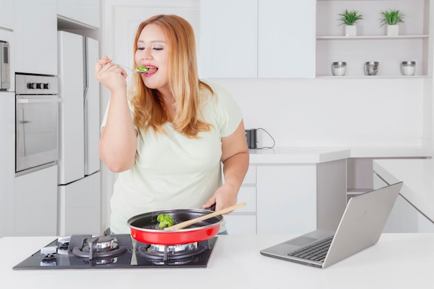 Hermosa mujer gorda probando comida en la cocina