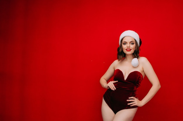 Foto hermosa mujer con gorro de papá noel y mono rojo sobre un fondo rojo concepto de año nuevo