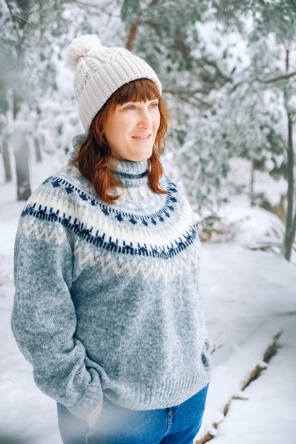 Hermosa mujer con un gorro y un suéter sobre un fondo de bosque nevado