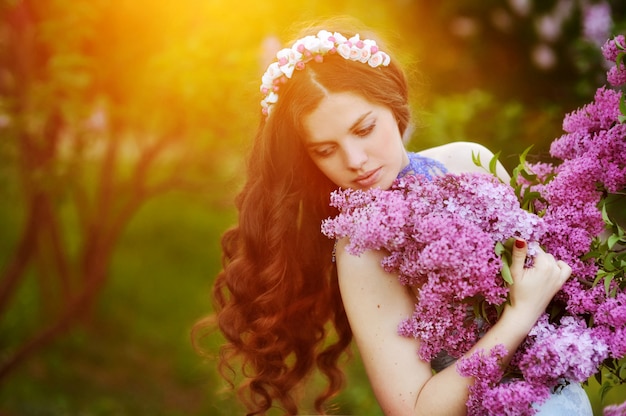 Hermosa mujer en guirnalda de flores con una flor lila en puesta de sol