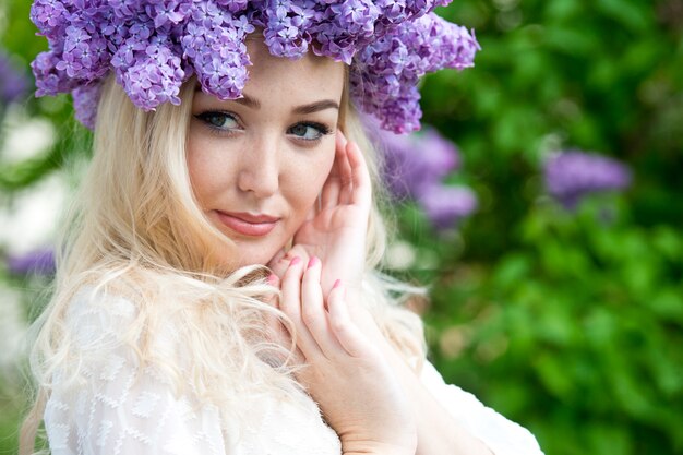 Foto hermosa mujer con guirnalda de flores lilas. chica en una corona de lilas en la primavera. corona de lilas. lila. jardinería