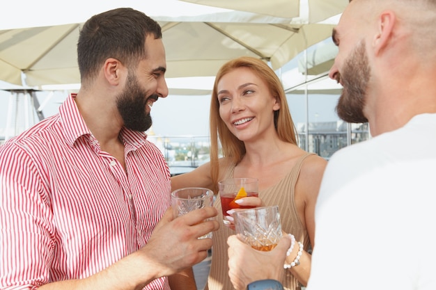 Hermosa mujer hablando con sus amigos varones con bebidas en una fiesta en la azotea