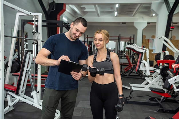 Hermosa mujer haciendo deportes intensos en el gimnasio con un joven y hermoso entrenador