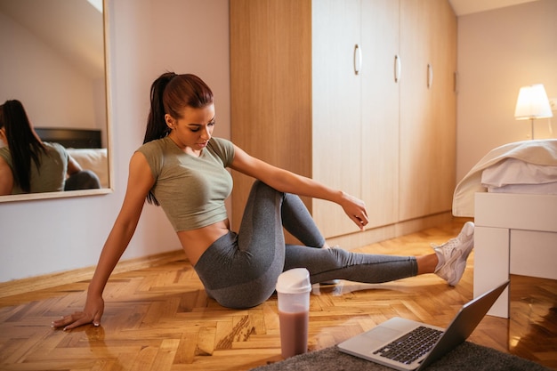 Hermosa mujer haciendo ejercicio en casa con su computadora portátil