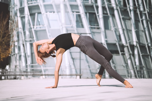 Hermosa mujer haciendo ejercicios de yoga fuera de la ciudad Niña practicando yoga al aire libre