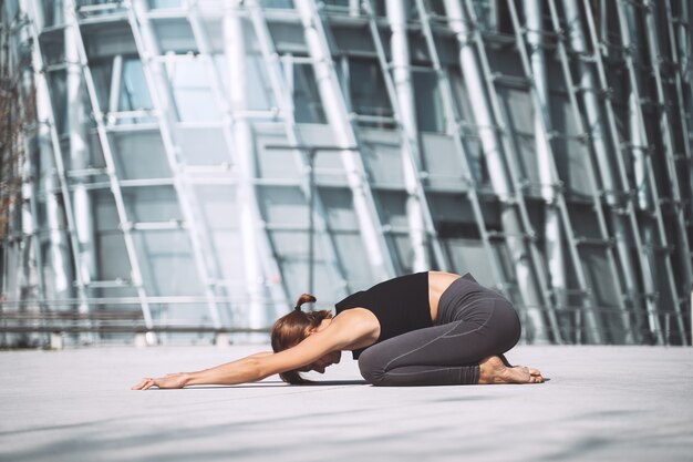 Hermosa mujer haciendo ejercicios de yoga fuera de la ciudad Niña practicando yoga al aire libre