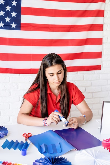 Hermosa mujer haciendo rosetas de papel de bricolaje de colores rojo y azul para celebrar el 4 de julio