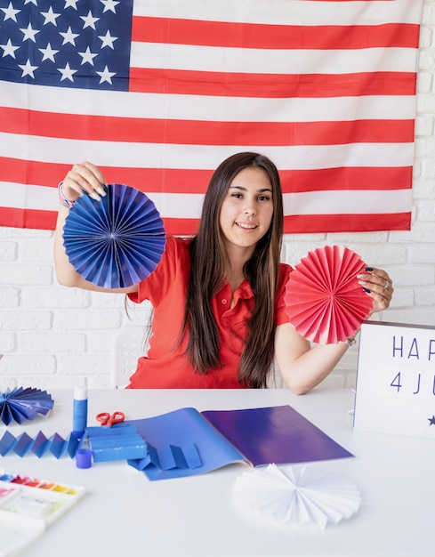 Foto hermosa mujer haciendo rosetas de papel de bricolaje de colores rojo y azul para celebrar el 4 de julio