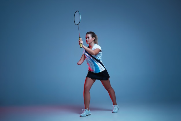 Hermosa mujer handicap practicando bádminton aislado sobre fondo azul en luz de neón. Estilo de vida de personas inclusivas, diversidad y equidad. Deporte, actividad y movimiento. Copyspace para anuncio.