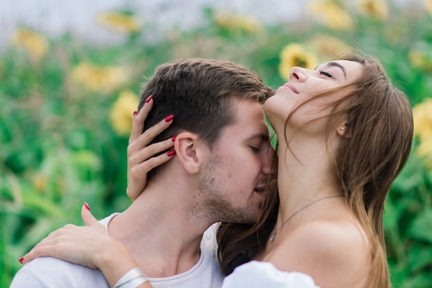 Hermosa mujer hermosa y elegante pareja masculina, rústica en un campo de girasol besos tiernos