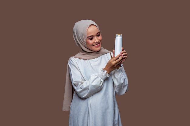 Hermosa mujer hijab sostenía la botella de champú con ambas manos mientras miraba la botella.