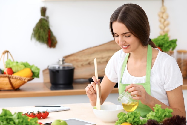 Hermosa mujer hispana está cocinando en la cocina. El ama de casa está probando ensalada fresca mientras está sentada en la mesa