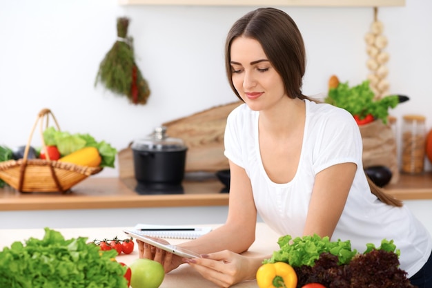 Hermosa mujer hispana está haciendo compras en línea por computadora de tableta y tarjeta de crédito o buscando en Internet una nueva receta. Que cocinar para una cena