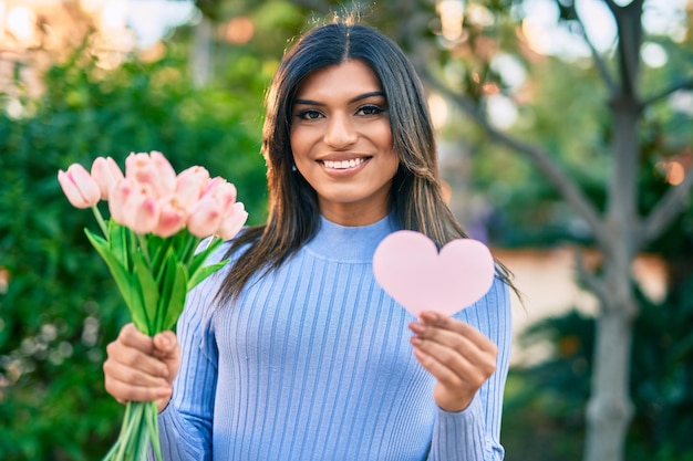 Hermosa mujer hispana con ramo de tulipanes y corazón rosa en el parque