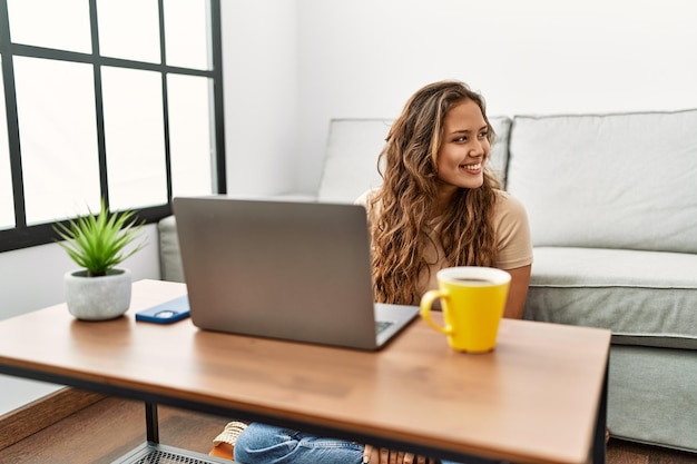 Hermosa mujer hispana usando computadora portátil en casa mirando de lado a lado con una sonrisa en la cara expresión natural riendo confiada