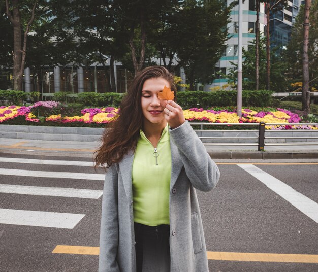 Hermosa mujer con hoja de otoño en la calle