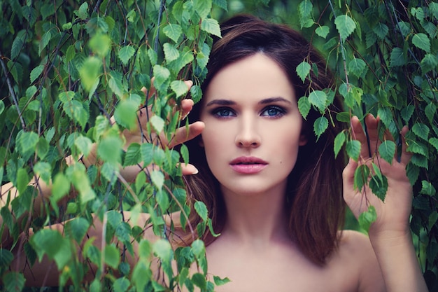 Hermosa mujer con hojas verdes al aire libre. Primer plano de la cara