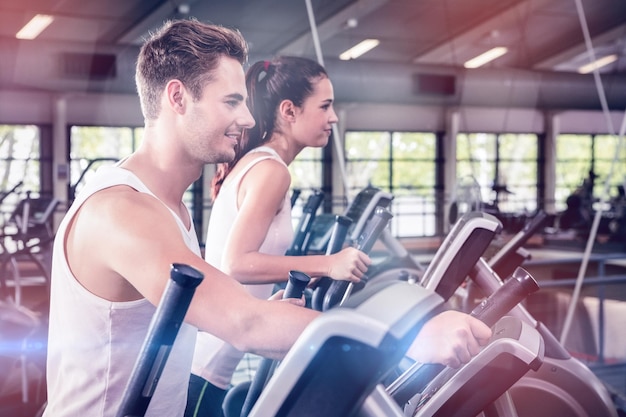 Hermosa mujer y hombre haciendo ejercicio en máquina elíptica en el gimnasio