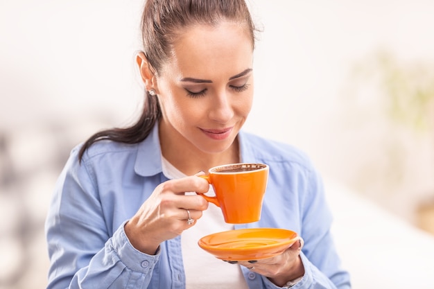 Hermosa mujer huele café recién hecho en una taza naranja.