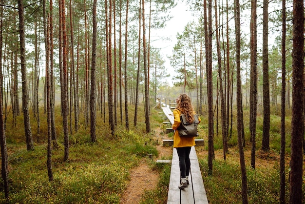 Foto hermosa mujer con impermeable amarillo camina por un sendero de madera en el bosque concepto de turismo recreativo